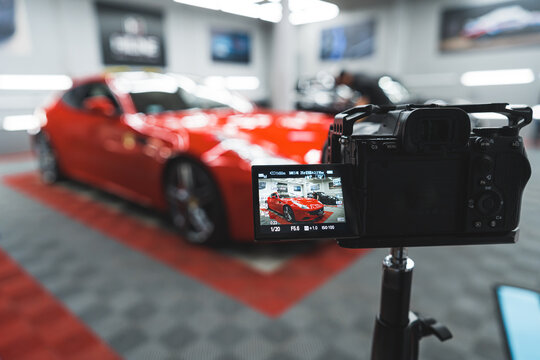 A photo camera taking pictures of red modern sports car in the car detailing salon. Blurred background. High quality photo
