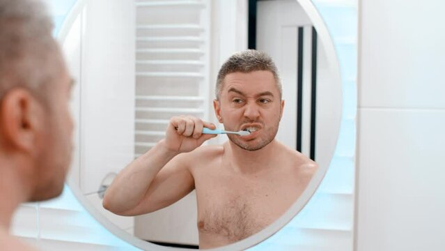 Young man brushing his teeth in bathroom. Morning men's procedures in the mirror