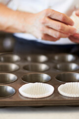 Fototapeta na wymiar Cupcake tray, person hands and baking in kitchen with muffin wrapper and cooking closeup in bakery. Prepare, paper cup and food with chef in restaurant, coffee shop or cafe with sweet cake or pastry