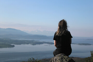 The girl sits with her back overlooking the sea and mountains, a tourist in Norway, loneliness