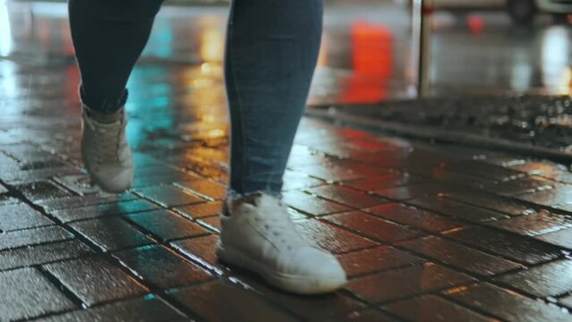 Legs of a girl taking a step into a puddle on the street of a night city
