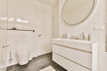 Fototapeta na wymiar a white bathroom with black tile flooring and a round mirror on the wall above the sink is an oval shaped mirror