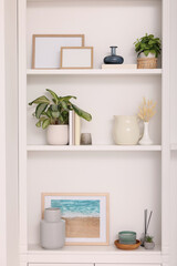 Interior design. Shelves with stylish accessories, potted plants and frames near white wall