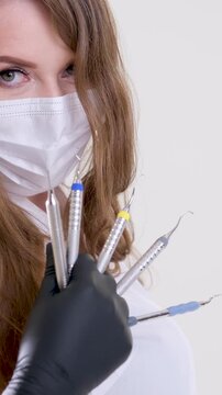 Beautiful woman dentist in white suit with a white mask with flowing hair holds in her hands scaler and curette Hand stretched forward selective 