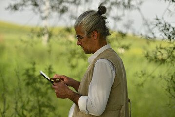 male business person drinking coffee talking on phone, doing analysis with tablet by the river in the park
