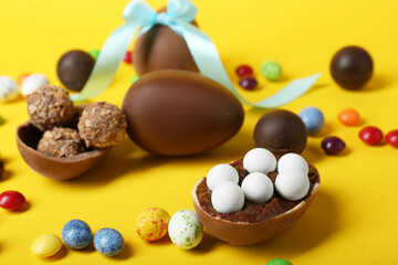 Tasty chocolate eggs and candies on yellow background
