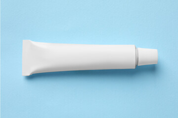 Tube of ointment on light blue background, top view. Space for text
