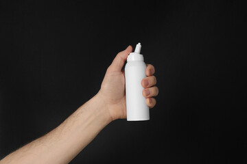 Man holding nasal spray on black background, closeup