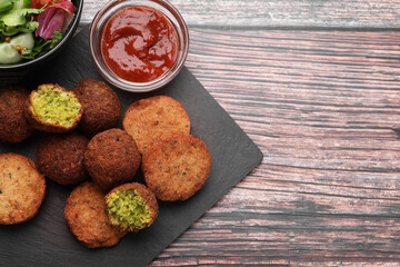 Delicious vegan cutlets and falafel ball served with sauce on wooden table, flat lay. Space for text