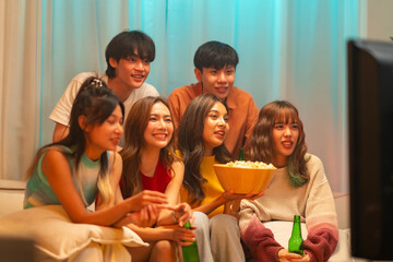 Group of Young Asian man and woman watching movie on television together in living room at home. Happy people friends enjoy and fun indoor activity lifestyle spending time together on holiday vacation