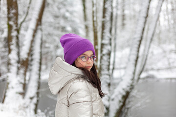 Fototapeta premium Portrait of a beautiful girl in a pink hat and glasses in the winter forest