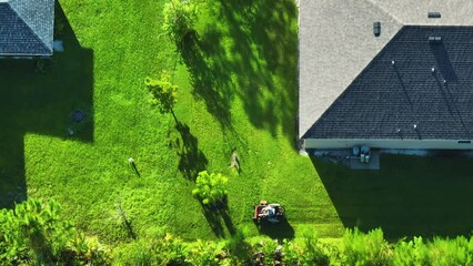 Top view of lawn mowing professional service worker cutting grass in summer with a lawn mower vehicle. Landscaping of rural home backyard