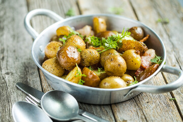 Baby young potatoes, bacon, parsley on a frying pan on a wooden background, close-up