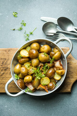 Baby young potatoes, bacon, parsley on a frying pan on a wooden background, close-up