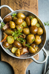 Baby young potatoes, bacon, parsley on a frying pan on a wooden background, close-up