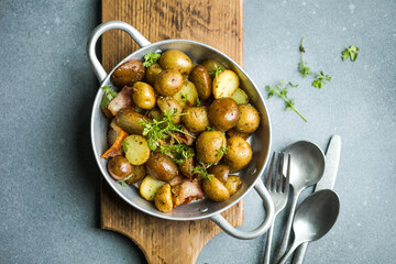 Baby young potatoes, bacon, parsley on a frying pan on a wooden background, close-up