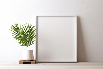 A clean empty white picture frame sitting next to a plant
