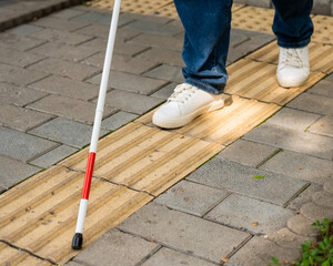 A blind woman walks outdoors using a cane along a tactile yellow tile.