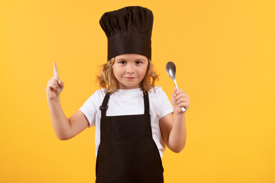 Cute kid boy cook with cooking spoon. Child wearing cooker uniform and chef hat preparing food on kitchen, studio portrait. Cooking, culinary and kids food concept.
