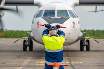 Rear view A signalman meets a passenger plane at the airport in front of propeller airplane. The...