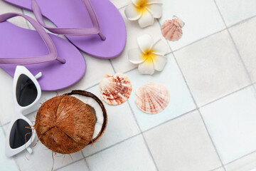 Composition with sunglasses, flip flops, seashells, coconut and plumeria flowers on tiled background