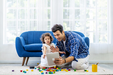 Modern Remote Communication Concept. Portrait of positive caucasian father making virtual video call with mother using tablet, while the little daughter was playing with colorful wooden blocks