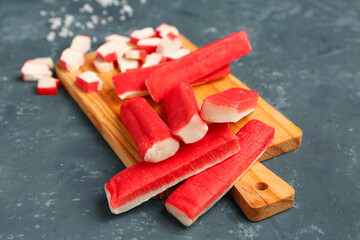 Wooden board with tasty crab sticks on green background © Pixel-Shot