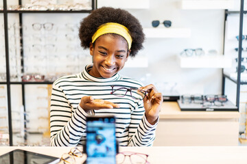 Young woman african american entrepreneur is fashion vlogger show glasses to cellphone and smiling...
