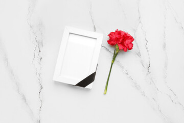 Photo frame with black ribbon and red carnation on white grunge background