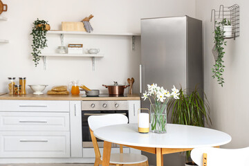 Interior of light kitchen with stylish fridge, counters, shelves, table and chairs