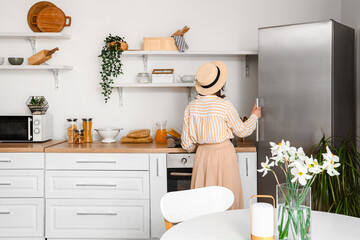 Young woman opening stylish fridge in kitchen