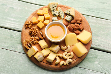 Board with pieces of tasty cheese, nuts and honey on light wooden background