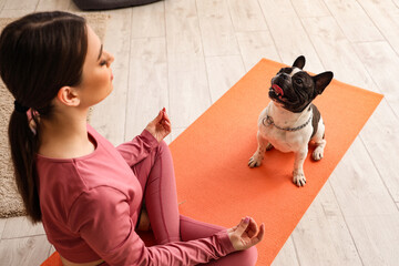 Sporty young woman with her French bulldog meditating at home