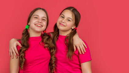 happy teen girls hugging on pink background