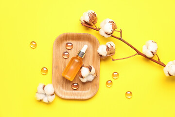 Composition with bottle of essential oil, glass stones and cotton flowers on yellow background