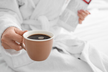 Woman in bathrobe holding cup of delicious coffee, closeup