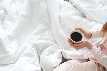 Woman holding cup of delicious coffee in bed