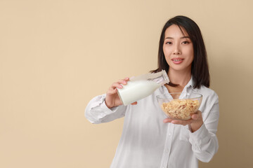 Young Asian woman with milk and cornflakes on beige background
