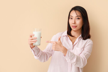 Beautiful Asian woman with glass of milk on beige background