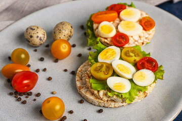 Rice crackers with quail eggs, tomatoes and lettuce on table, closeup