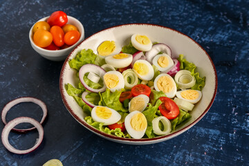 Tasty salad with quail eggs, tomatoes, onion and lettuce on dark blue background