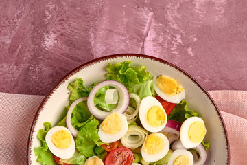 Tasty salad with quail eggs, tomatoes, onion and lettuce on pink background, closeup