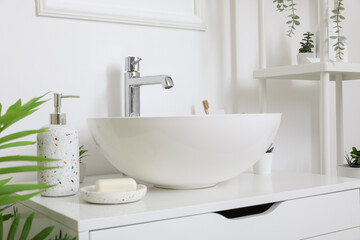 Sink bowl and bath accessories on chest of drawers in bathroom