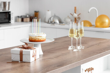 Birthday cake with gift and glasses of champagne on table in kitchen