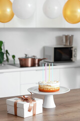 Stand with Birthday cake and gift on table in kitchen