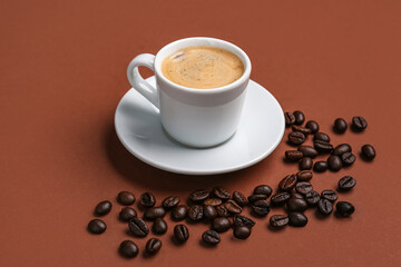 Cup of hot espresso and coffee beans on brown background