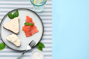 Plate of tasty sandwiches with cream cheese and fish on blue background