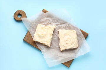 Wooden board of tasty toasts with cream cheese on blue background