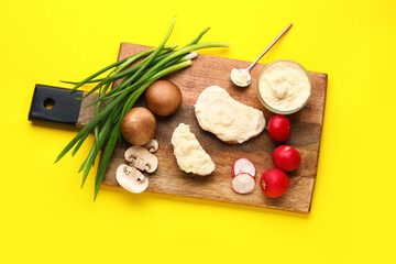 Wooden board of tasty sandwiches with cream cheese and vegetables on yellow background