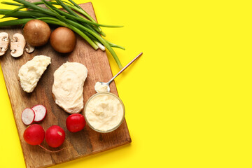 Wooden board of tasty sandwiches with cream cheese and vegetables on yellow background
